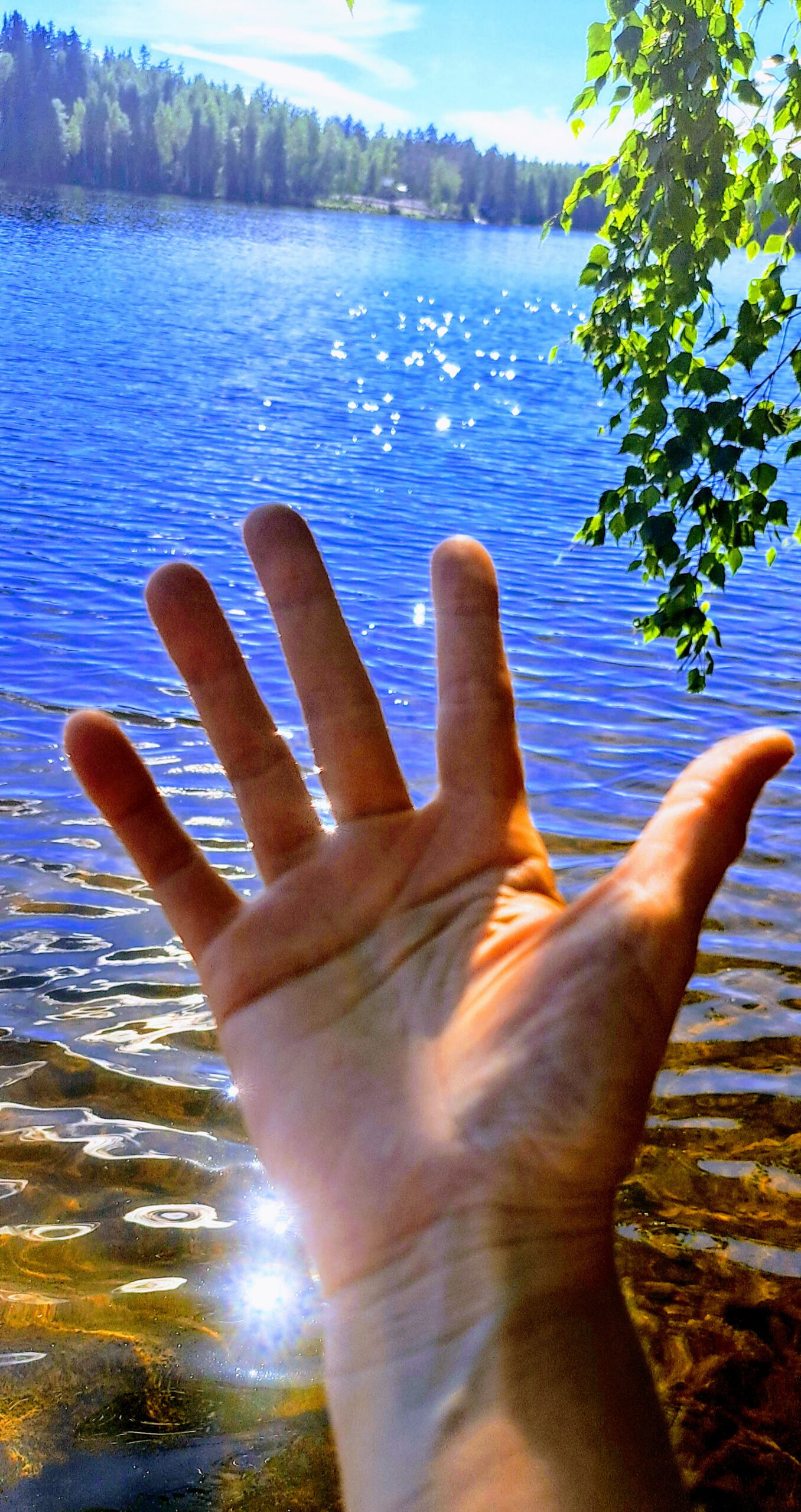 Hand im Wasser mit Lichtreflexen an einem See in Finnland